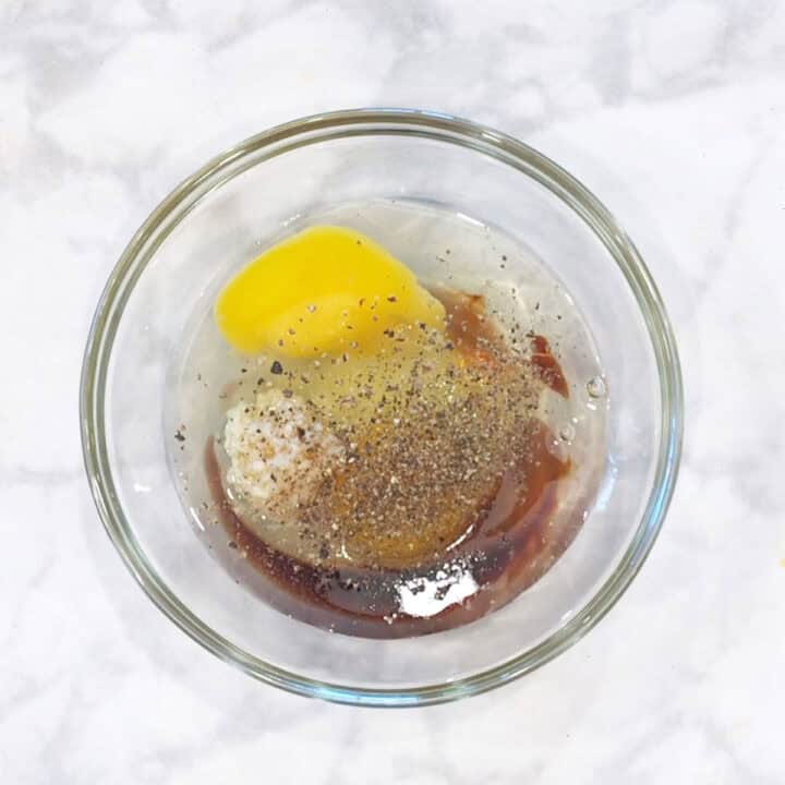 A bowl with eggs, soy sauce, black pepper, and garlic.