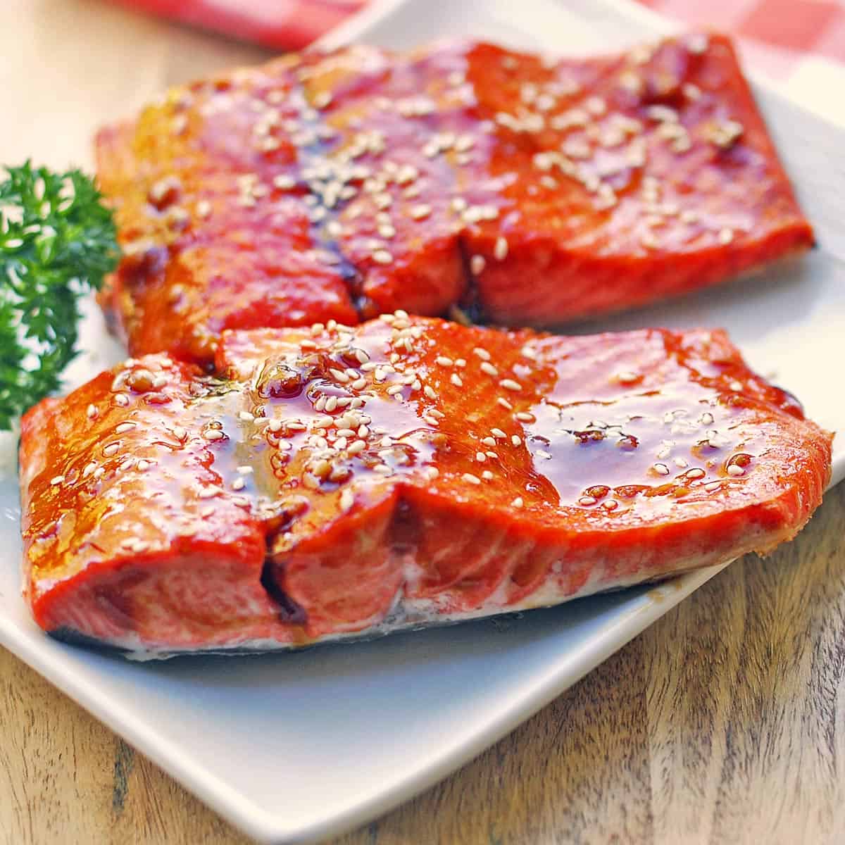 Two teriyaki salmon fillets are served on a white plate.