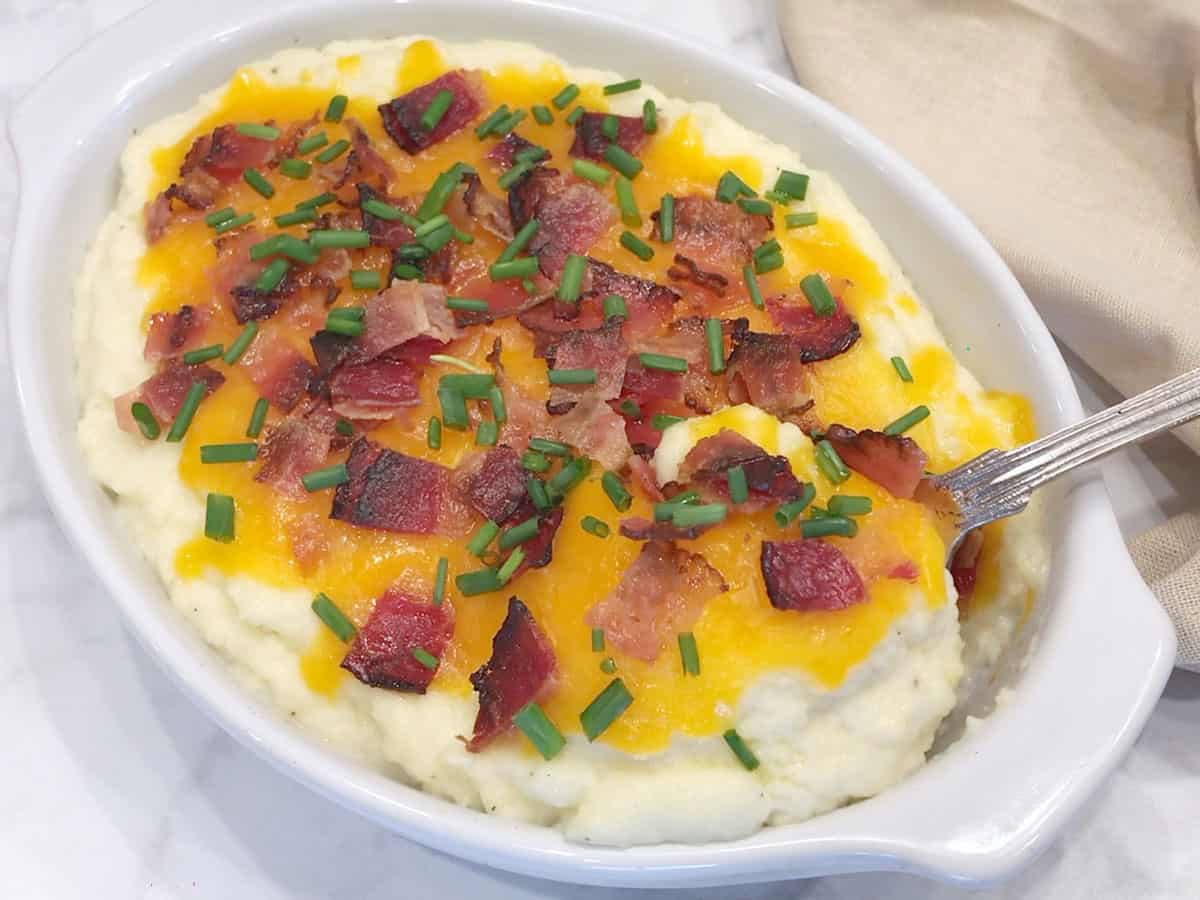 Loaded mashed cauliflower is served with a spoon.