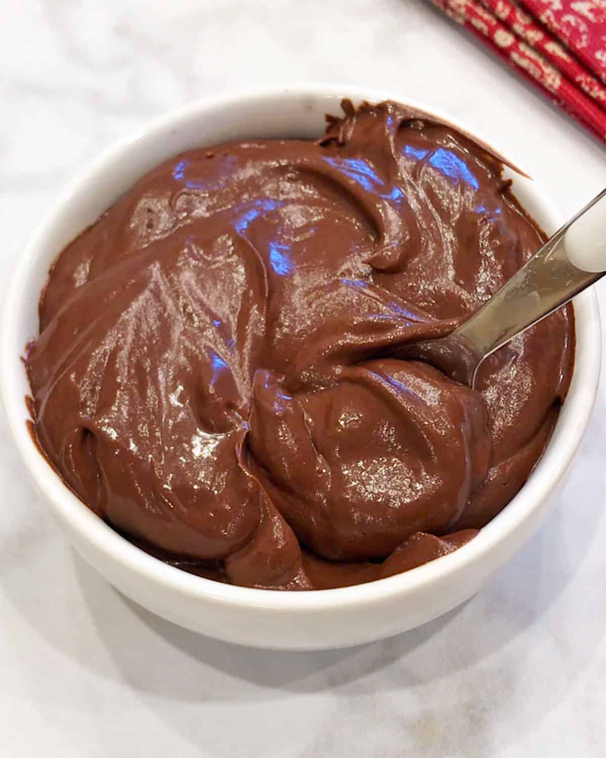 Avocado chocolate mousse is served in a white bowl with a spoon.