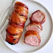 Bacon wrapped pork tenderloin is served on a white plate.