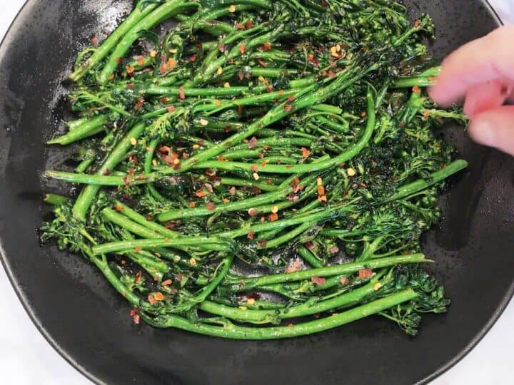Garnishing the broccolini with red pepper flakes.