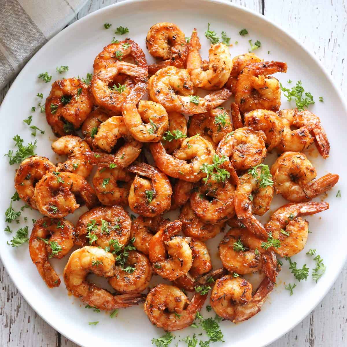 Sauteed shrimp are served on a white plate, garnished with chopped parsley.